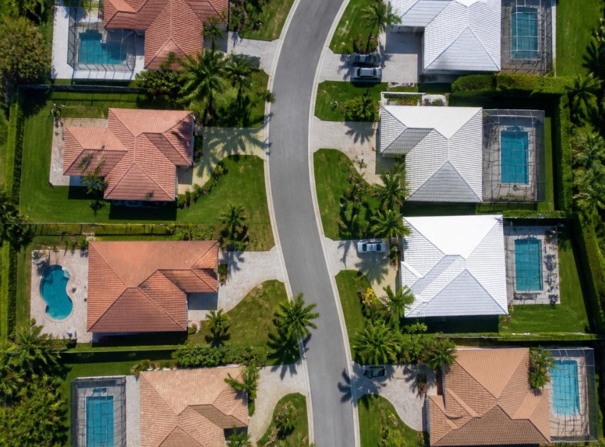 Aerial view of a curving street of homes with backyard pools, several under screen enclosures